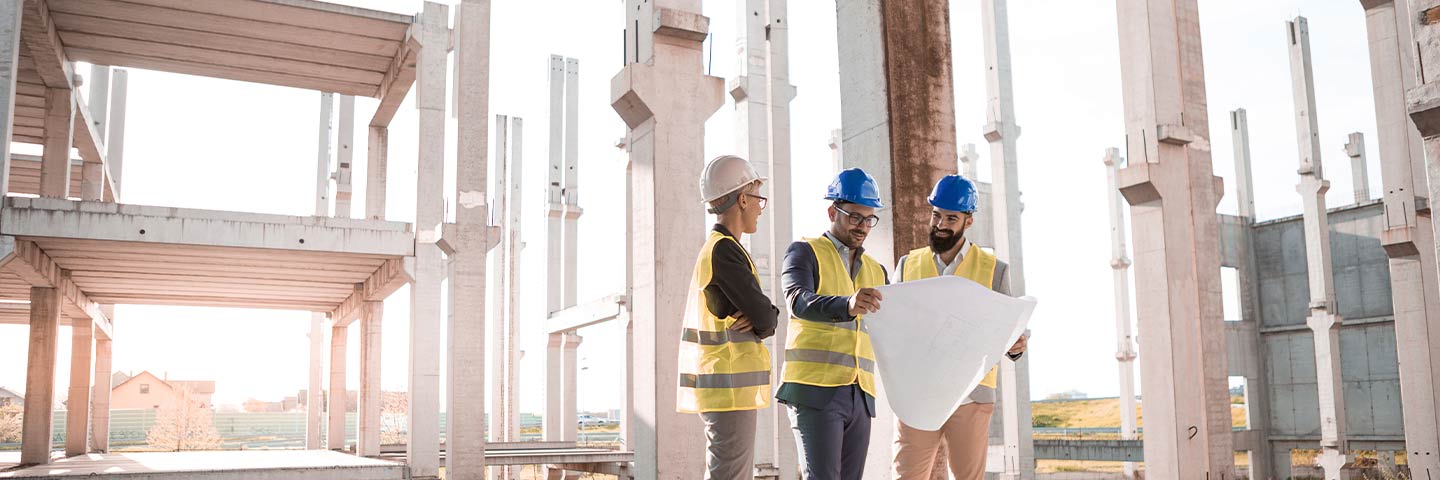 three engineers in hardhats looking at blueprints of construction project on site